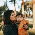 woman in black jacket carrying baby in orange jacket